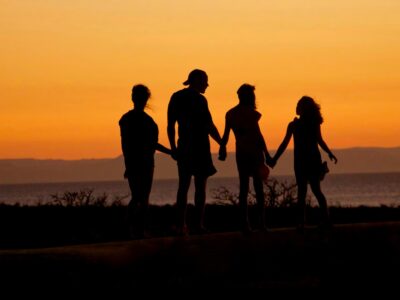 silhouette of man standing beside shore under brown sky during daytime