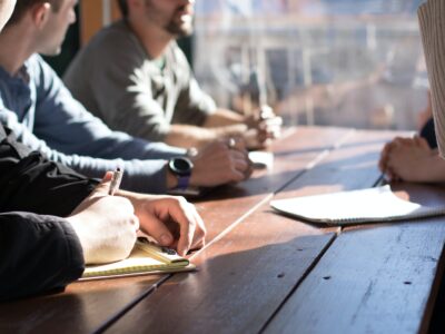 people sitting on chair in front of table while holding pens during daytime